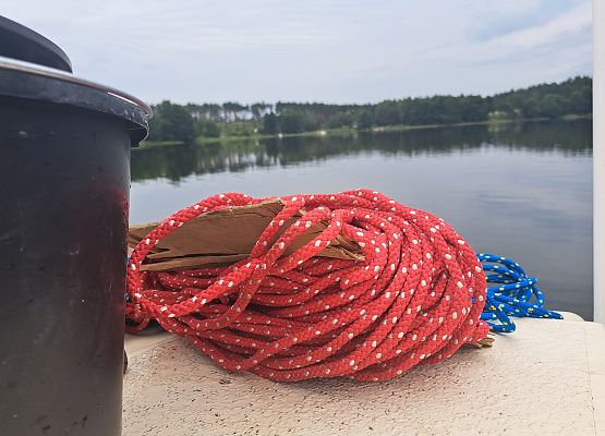 Wiadro i czerwona lina na łodzi, w tle widok na jezioro, fot. M.greinke