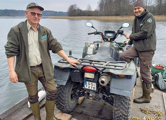 Pracownicy WPK przewożący sprzęt na platformie na jeziorze.