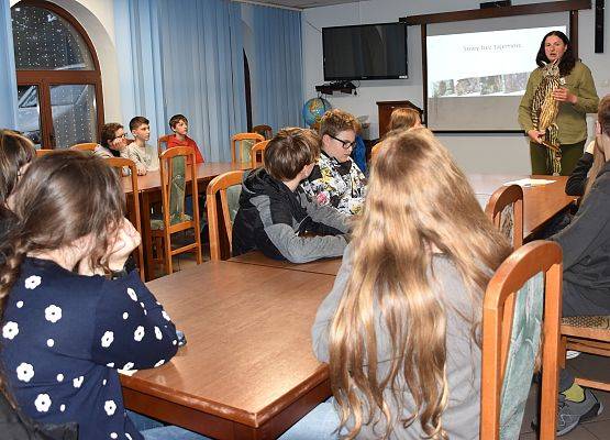 Młodziez siedząca przy stołach w sali edukacyjnej podczas wykładu o sowach.